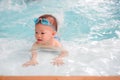 Cute little Asian 18 months toddler boy child in trunks wear swimming goggles learn to swim at indoor pool Royalty Free Stock Photo