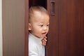 Cute little Asian 18 months / 1 year old toddler baby boy child wearing white sweater is hiding in the closet at home Royalty Free Stock Photo
