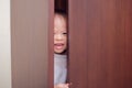 Cute little Asian 18 months / 1 year old toddler baby boy child wearing white sweater is hiding in the closet at home Royalty Free Stock Photo