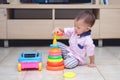 Cute little Asian 18 months / 1 year old toddler boy play with educational colorful plastic pyramid toy / stacking ring toy in liv