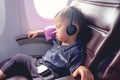 Toddler boy sitting with safety belt on wearing headphones while traveling in airplane