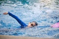 Cute little Asian school boy child in swimming goggles and swimming suit uses a foam pad to practice swimming in a swimming pool Royalty Free Stock Photo
