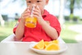 Asian 1 year old toddler baby boy child sitting in high chair holding & drinking tasty orange juice Royalty Free Stock Photo