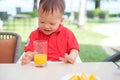 Asian  toddler baby boy child sitting in high chair holding & drinking tasty orange juice / cold drink in a Royalty Free Stock Photo