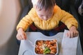 Cute little Asian 2 years old toddler baby boy child wearing yellow jacket eating food pasta during flight on airplane Royalty Free Stock Photo