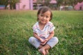 Cute little Asian 1 - 2 years old toddler baby girl child smiling at camera, barefoot practices yoga & meditating outdoors on