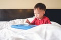 Cute little Asian 2-3 years old toddler boy child sitting in bed watching a video from tablet pc