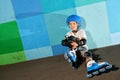 Cute little athletic boy on roller sitting against the blue graffiti wall