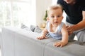 Cute little baby boy with big blue eyes try stand up on sofa, father help him Royalty Free Stock Photo