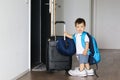 Cute little baby boy in fathers shoes and with big backpack holding suitcase staying near open door ready to travel leaving home. Royalty Free Stock Photo