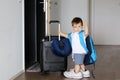 Cute little baby boy in fathers sneakers and with big backpack holding suitcase and waving goodbye staying at open door ready to t Royalty Free Stock Photo