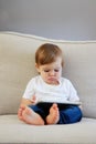 Cute little baby boy with funny face expression watching cartoons on digital tablet sitting on sofa at home. Royalty Free Stock Photo