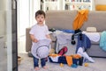 Cute little baby boy with funny surprised face expression holding hat in hands helping to pack suitcase packing clothes and toys f Royalty Free Stock Photo