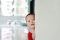 Cute little baby boy hide behind a corner room. Baby playing peekaboo game indoor. What a surprise