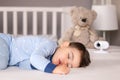 Cute little baby boy in light blue pajamas sleeping peacefully on bed at home with baby monitor camera and soft teddy bear toy at Royalty Free Stock Photo