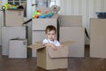 Cute little baby boy sitting inside cardboard box with big boxes full of toys on background, moving out