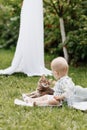 Cute little baby boy sitting on white blanket on green grass in summer, on a Sunny day, playing with a cat. Selective Royalty Free Stock Photo