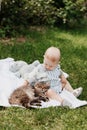 Cute little baby boy sitting on white blanket on green grass in summer, on a Sunny day, playing with a cat. Selective Royalty Free Stock Photo