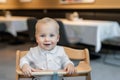 Cute little baby boy in white polo t-shirt sitting in wooden baby chair and laughing at cafe indoors. Portrait of Royalty Free Stock Photo