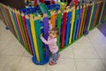 A cute little baby climbs at the colorful fence of a children`s playroom, looks in the camera and wants to play inside Royalty Free Stock Photo