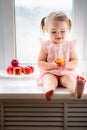 Cute little baby girl eats peaches on the window Royalty Free Stock Photo