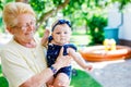 Cute little baby girl with grandmother on summer day in garden. Happy senior woman holding smiling child on arm Royalty Free Stock Photo