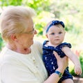 Cute little baby girl with grandmother on summer day in garden. Happy senior woman holding smiling child on arm.. Royalty Free Stock Photo