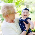 Cute little baby girl with grandmother on summer day in garden. Happy senior woman holding smiling child on arm Royalty Free Stock Photo