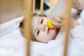Cute little baby girl holding bottle with formula mild and drinking. Child in baby cot bed before sleeping Royalty Free Stock Photo