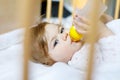 Cute little baby girl holding bottle with formula mild and drinking. Child in baby cot bed before sleeping Royalty Free Stock Photo