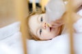 Cute little baby girl holding bottle with formula mild and drinking. Child in baby cot bed before sleeping Royalty Free Stock Photo