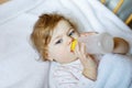 Cute little baby girl holding bottle with formula mild and drinking. Child in baby cot bed before sleeping Royalty Free Stock Photo