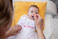 Cute little baby girl lying on the bed and eating rice soup with spoon. Mother feeding her baby girl. The baby girl is four months Royalty Free Stock Photo