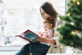 Cute little baby girl in pink dress with her mother young woman reading book in room at home, Christmas time at home, happy New Royalty Free Stock Photo