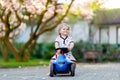 Cute little baby girl playing with blue small toy car in garden of home or nursery. Adorable beautiful toddler child