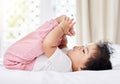 Cute little baby girl playing with her feet,lying on the bed in her bedroom. Small hispanic baby holding and looking at Royalty Free Stock Photo