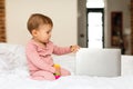 Cute little baby girl sitting on bed and touching laptop computer, bedroom interior, free copy space Royalty Free Stock Photo