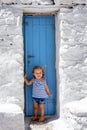 A cute, little baby girl stands on a traditional blue door, Mykonos island, Greece