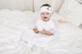 Cute little baby girl in white clothes, sitting on bed, playing with toy Royalty Free Stock Photo