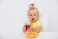 Cute little baby girl 1 year old eating cereal flakes and drinking juice or compote from a bottle at the table isolated on white Royalty Free Stock Photo