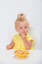 Cute little baby girl 1 year old in yellow t-shirt eating cereal flakes at the table isolated on white background Royalty Free Stock Photo