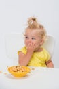 Cute little baby girl 1 year old in yellow t-shirt eating cereal flakes at the table isolated on white background Royalty Free Stock Photo