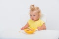 Cute little baby girl 1 year old in yellow t-shirt eating cereal flakes at the table isolated on white background Royalty Free Stock Photo