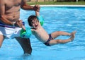Cute little baby on inflatable sleeves playing with his father in a swimming pool during a hot summer morning