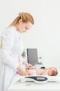 Cute little baby lying on scales, medical checkup in clinic, copy space. Young female blonde pediatrician doctor examines baby Royalty Free Stock Photo