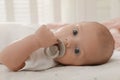 Cute little baby with pacifier lying on bed at home, closeup Royalty Free Stock Photo