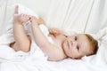 Cute little baby playing with own feet after taking bath. Adorable beautiful girl wrapped in white towels Royalty Free Stock Photo