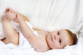 Cute little baby playing with own feet after taking bath. Adorable beautiful girl wrapped in white towels