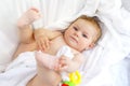 Cute little baby playing with toy rattle and own feet after taking bath. Adorable beautiful girl wrapped in white towels Royalty Free Stock Photo