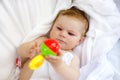 Cute little baby playing with toy rattle and own feet after taking bath. Adorable beautiful girl wrapped in white towels Royalty Free Stock Photo